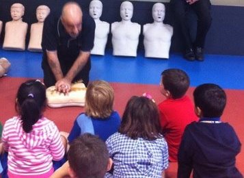 An instructor demonstrating CPR to a group of children during onsite first aid training.